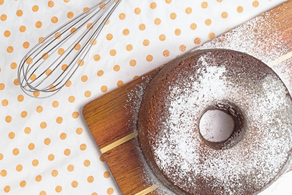 Delicious homemade bundt cake with powdered sugar on a wooden board with a whisk.